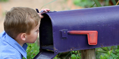 Boy about 3 years old looking into blue mailbox