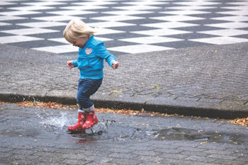 Young child wearing wellies, stomps in puddle