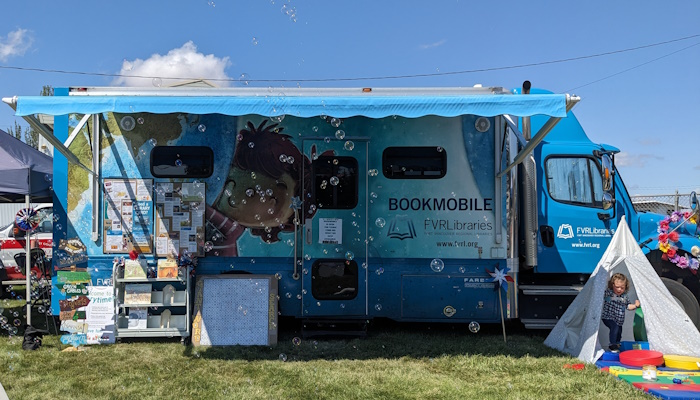 The bookmobile open for business with awning, a small tent and bubbles flying through the air