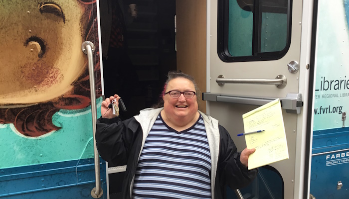 Judy exitedly holds up the keys to the new bookmobile while standing in the patron door