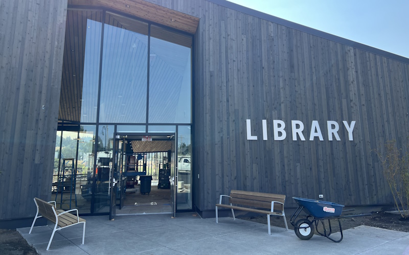 Front entrance with tall glass windows, outdoor benches, and LIBRARY spelled out on the wall