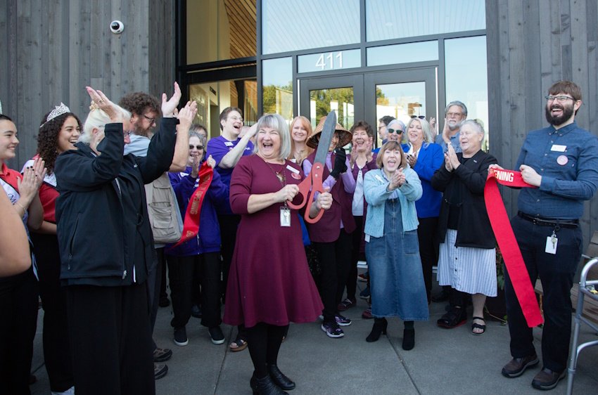 A large group of laughing people surround the now cut ribbon at Woodland Community Library's front entrance