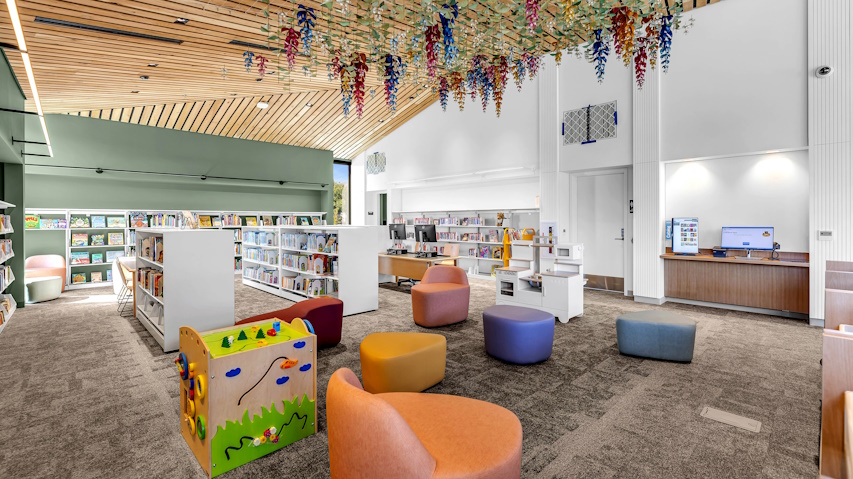 Children's area of the library with colorful chairs, low book shelves, and colorful artwork dangling from the ceiling