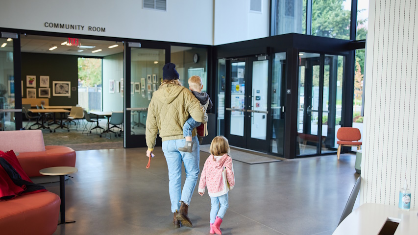 Woman with toddler in arms and preschooler walking along as they leave the library