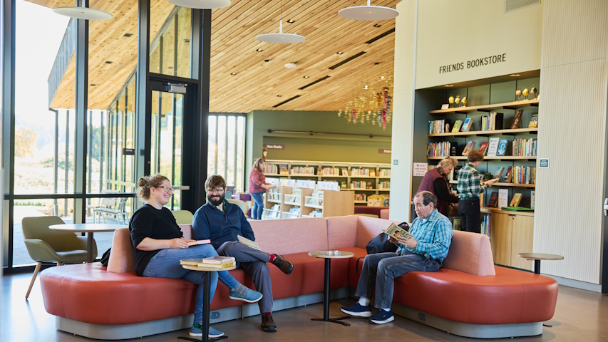 A few people converse and read on low, sofas near the library's entrance with the Friends' Book Store in the background