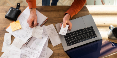 laptop computer surrounded by financial papers hand holding credit card