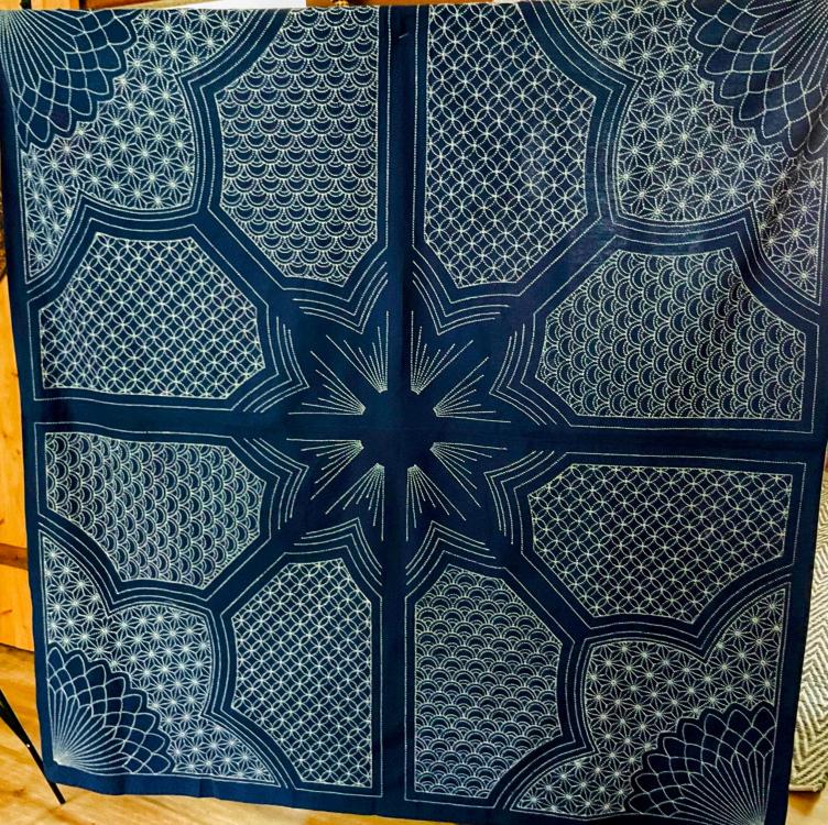 Dark blue and white design on cloth with hollow starburst like center with segments containing different repeating patterns radiating into decorative corners