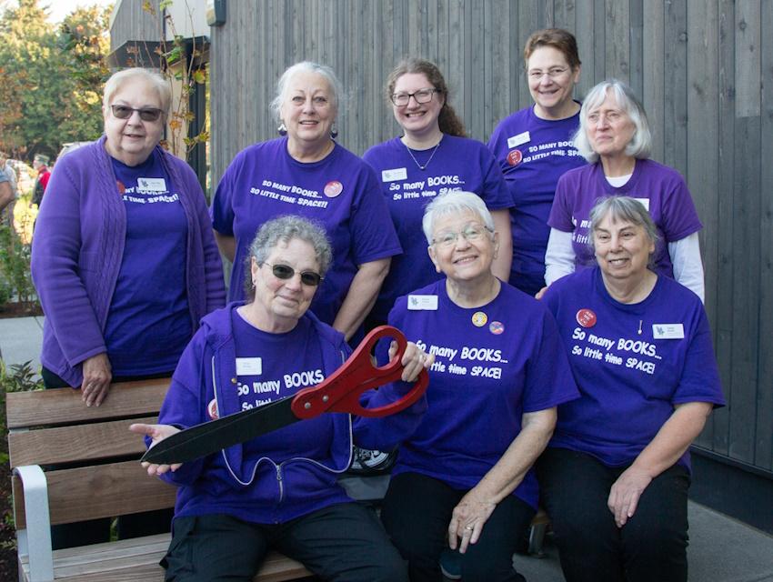 Members of the Woodland Friends of the Library group, all matching in purple shirts, pose with the giant scissors used for the grand opening