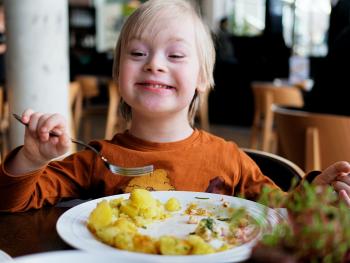 A smiling child holds a fork over a plate of food. 