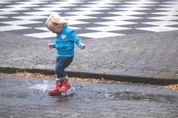 Young child wearing wellies, stomps in puddle