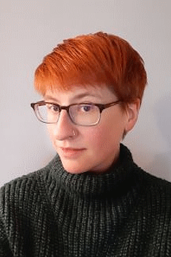 Woman with red hair, glasses, wearing black sweater