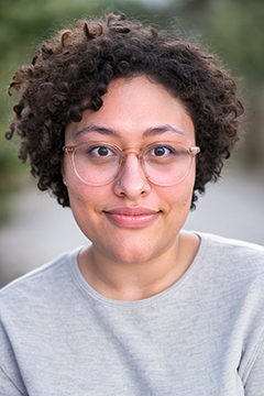 Person with dark curly hair, glasses, gray sweater