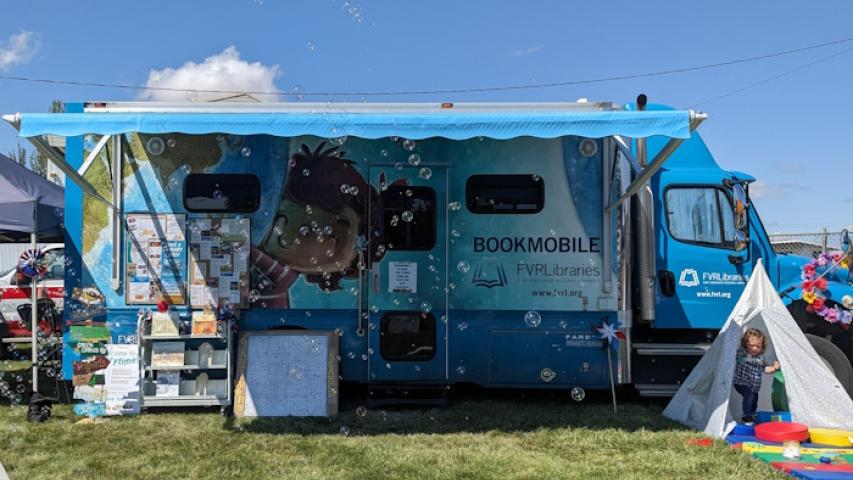 The bookmobile open for business with awning, a small tent and bubbles flying through the air