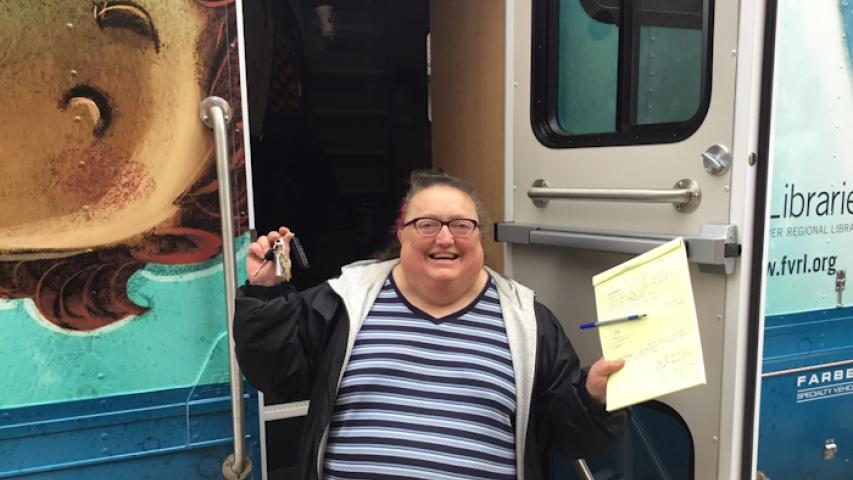 Judy exitedly holds up the keys to the new bookmobile while standing in the patron door