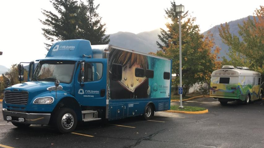 The new, blue bookmobile parked in the lot with the retiring, light colored one in the back