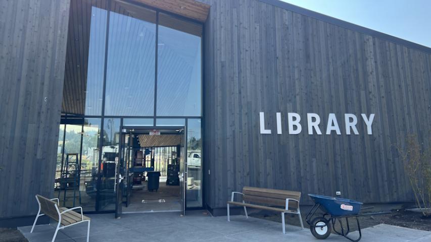 Front entrance with tall glass windows, outdoor benches, and LIBRARY spelled out on the wall