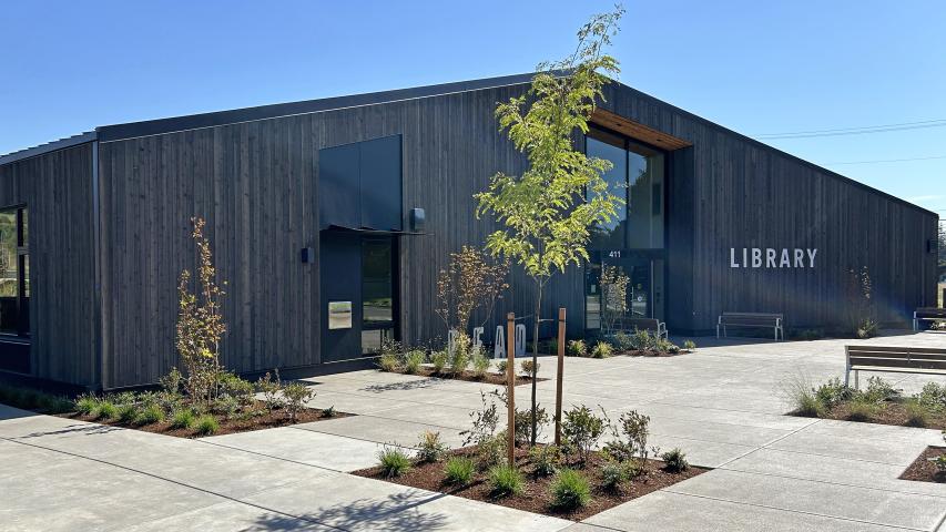 A wide view of the whole front of the new building with landscaping and parking.