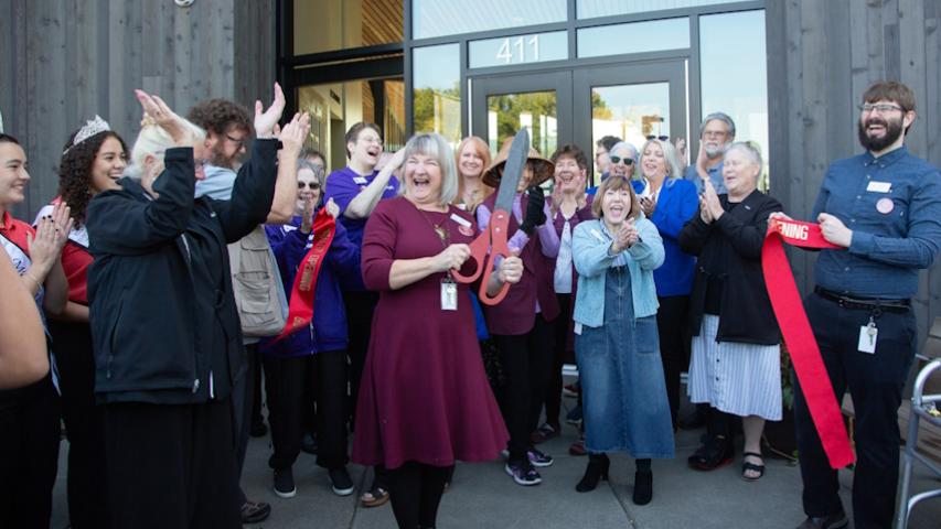 A large group of laughing people surround the now cut ribbon at Woodland Community Library's front entrance