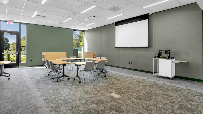 Large, open space with table and chairs, viewing screen on wall, and 3-D Printer on cart