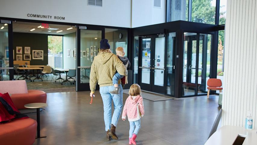 Woman with toddler in arms and preschooler walking along as they leave the library