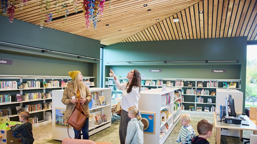 Two women with children looking up in the Children's room at the artwork hanging from the ceiling